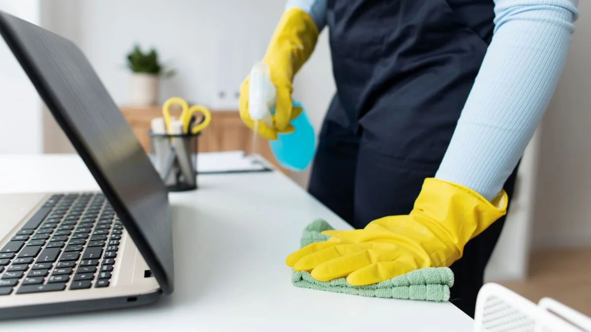 Een persoon met handschoenen die de oppervlakte van een meubel desinfecteerd.
